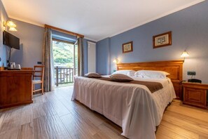 Un dormitorio con cama, mesitas de noche, televisor y vistas al exterior.