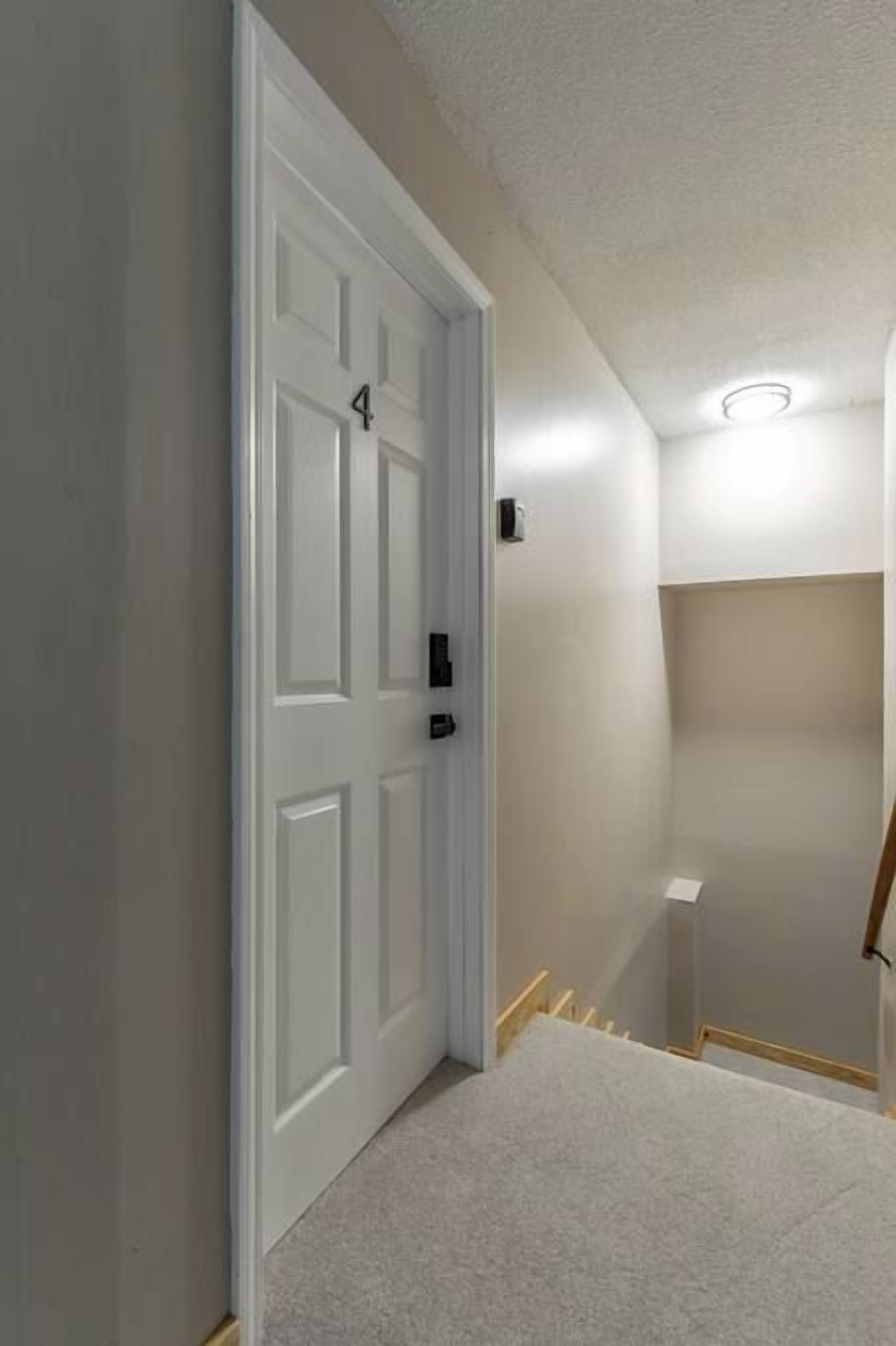 A hallway with a white door marked with the number 4, a light switch, and a small shelf.