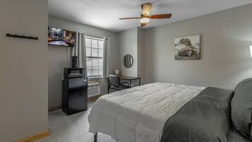 Un dormitorio con cama, escritorio, silla, ventilador de techo y ventana.