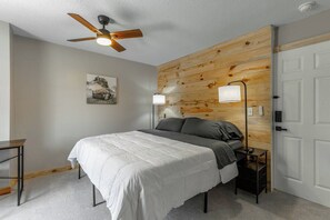A bedroom with a bed, a ceiling fan, a nightstand, and a door.