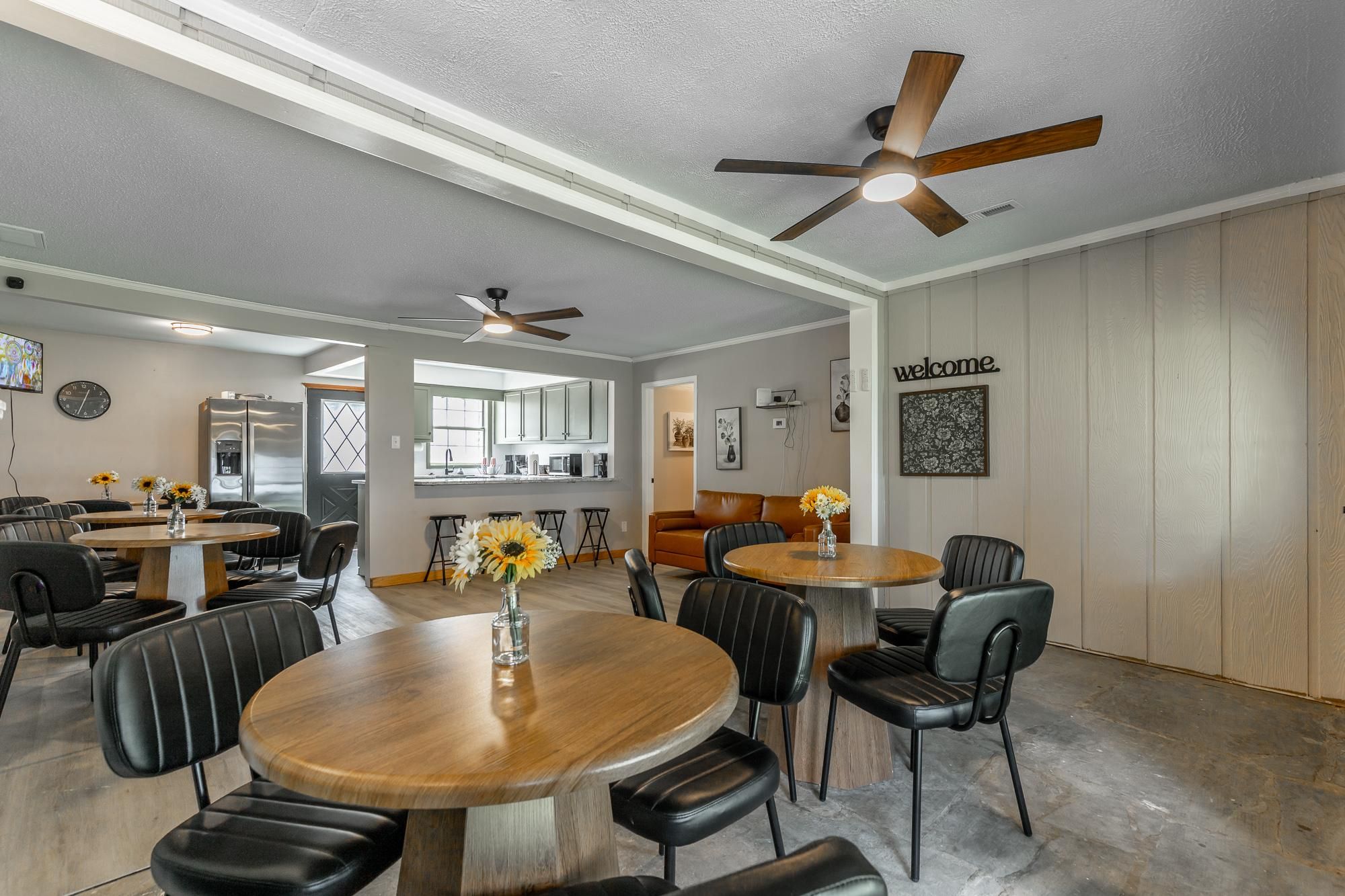 Round wooden tables with black leather chairs fill the dining area, lit by ceiling fans with wood blades.