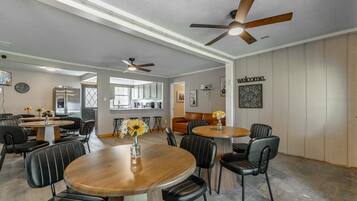Round wooden tables with black leather chairs fill the dining area, lit by ceiling fans with wood blades.