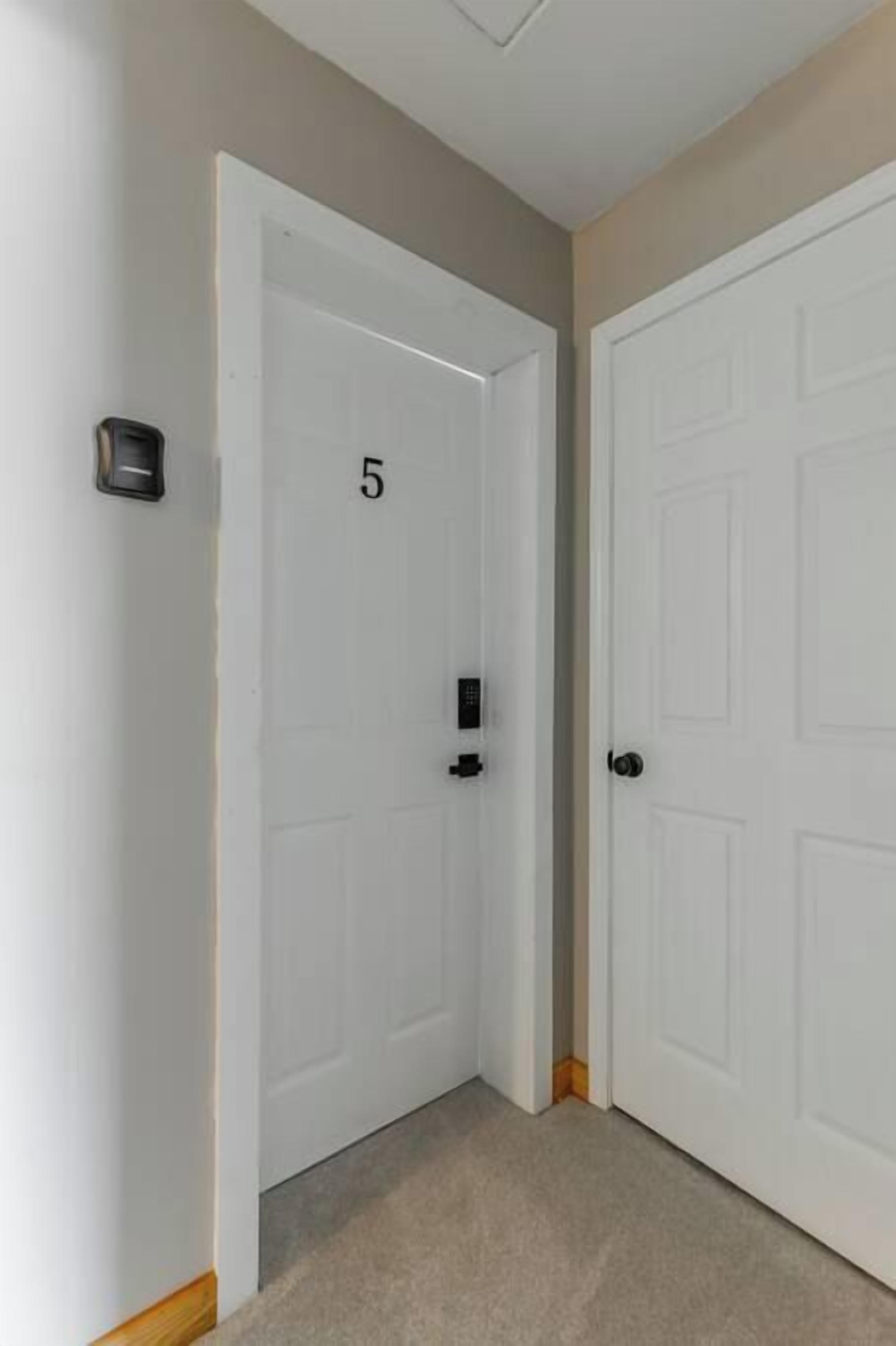 A hallway with two white doors, one marked with the number 5, and a doorbell on the wall.