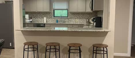 Una cocina con una isla central, taburetes de bar, luces colgantes y un ventilador de techo.