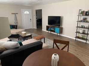 Ein Wohnzimmer mit Sofa, Couchtisch, TV-Schrank und Esstisch.