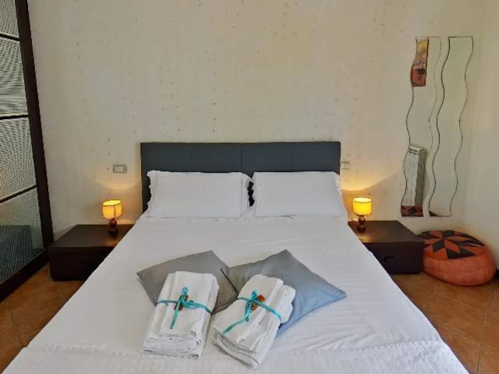Una camera d'albergo con un letto, due lampade ai comodini, un quadro e un poggiapiedi.