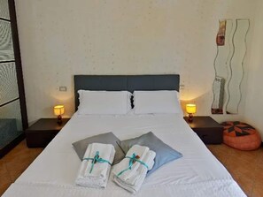 Una camera d'albergo con un letto, due lampade ai comodini, un quadro e un poggiapiedi.