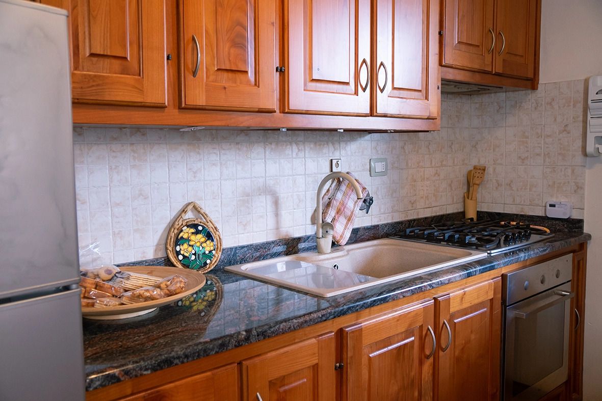 Una cucina con mobili in legno, un piano di lavoro in granito, un lavello in acciaio inossidabile e un fornello.