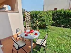 Una veranda esterna con un tavolo rotondo e quattro sedie, circondata da un prato curato e un siepe.