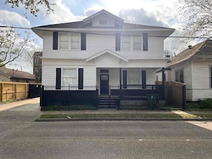 A two-story residential building with a front porch, a black metal fence, and a driveway. - East Downtown Loft + Gated Parking (Houston)