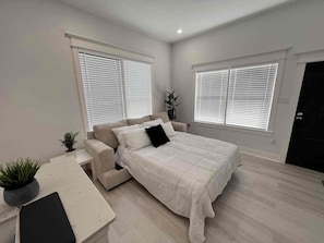 A bedroom with a bed, a chair, a desk, and two windows with blinds. - East Downtown Loft + Gated Parking (Houston)