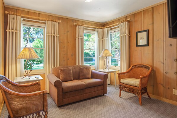 A room with a brown sofa, two wicker chairs, a small table, and a lamp.
