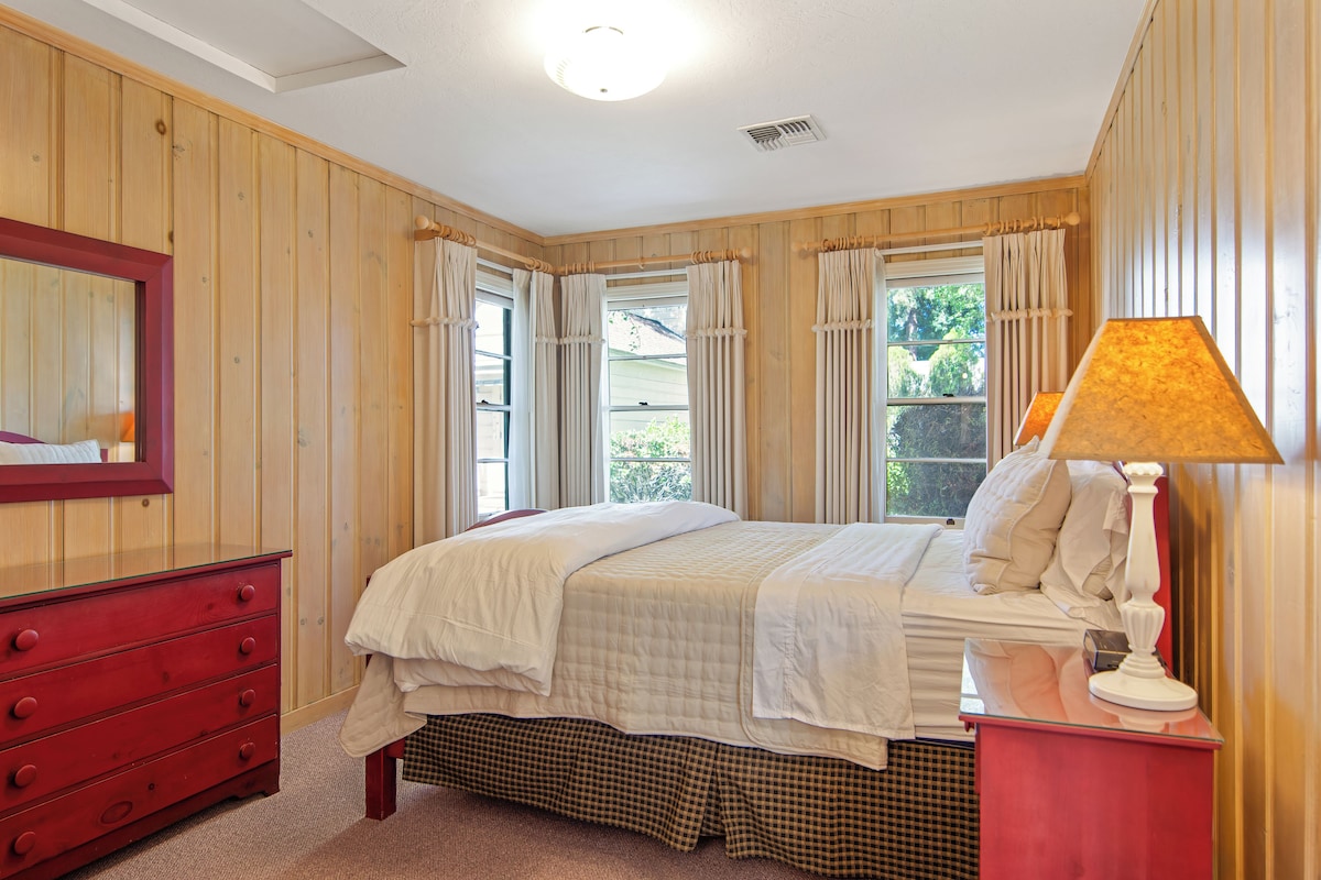 Un dormitorio con cama, cómoda, lámpara y ventana con cortinas.