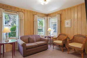 A room with a brown sofa, two wicker chairs, a small table with a lamp, and a framed picture on the wall. - Hideaway Cottages  (Calistoga)