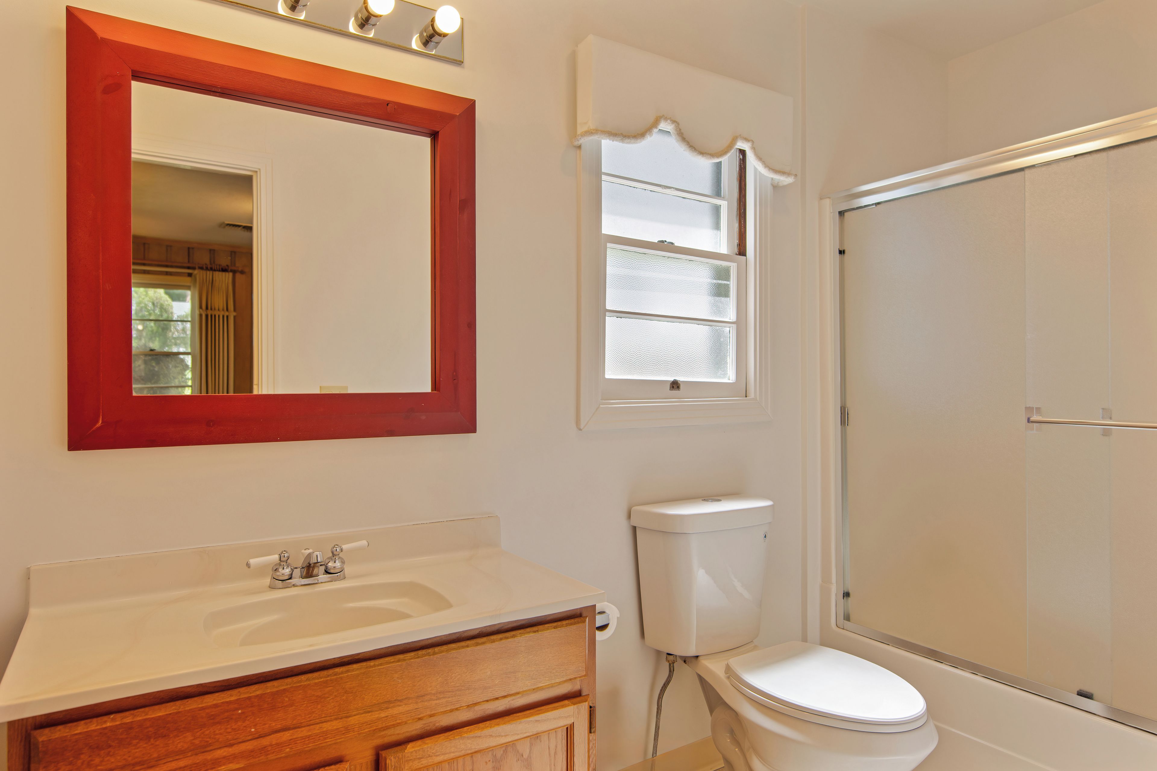 A bathroom with a wooden vanity, a white toilet, a shower enclosure, and a mirror with lights.