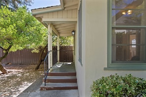 A covered porch with a wooden fence and a tree in the background.