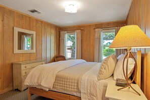 A bedroom with a bed, bedside table, lamp, and a window with curtains. - Hideaway Cottages  (Calistoga)