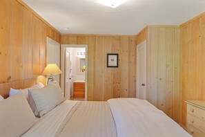 A bedroom with wooden paneling, a bed with white bedding, a bedside lamp, and a framed picture on the wall.