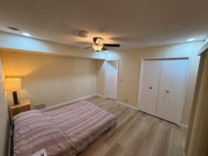 Ein Schlafzimmer mit einem Bett, einem Deckenventilator, einem Nachttisch und einer Tür.