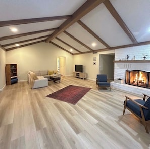 A spacious living room with a fireplace, wooden beams on the ceiling, and a television. - New renovated 3 bed 3 bath with Castle Rock view, outdoor fire pit -New in vrbo (Sedona)