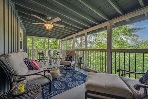 A covered porch with seating, a ceiling fan, and a view of trees. - Sunrise Surprise - Guest Favorite (Lake Lure)