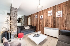 Una sala de estar moderna con una pared de acento de piedra, un sofá gris, una mesa de centro blanca y una pared de madera con ilustraciones de animales.