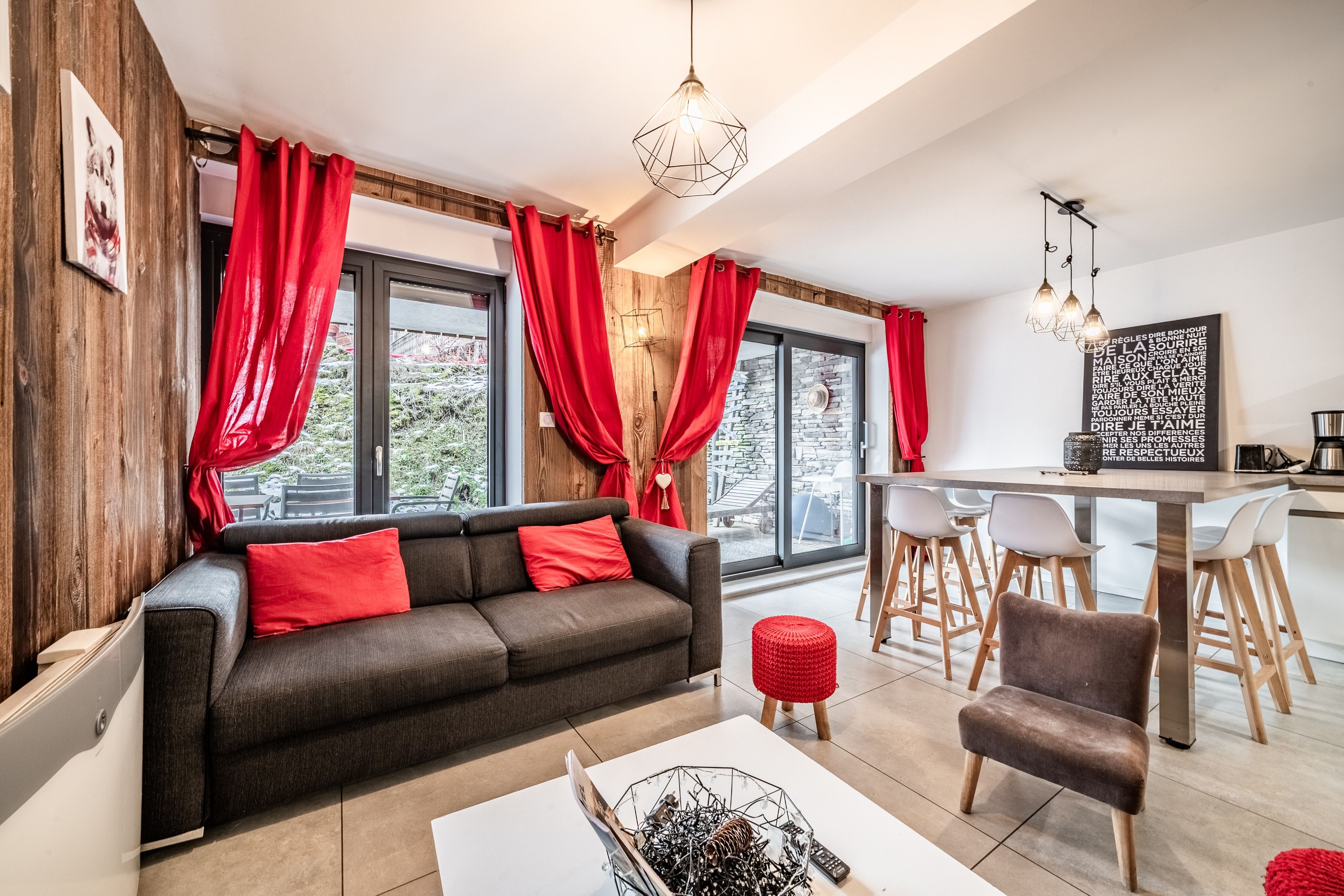 A modern living room with a sofa, red cushions, a coffee table, and a dining area with a table and chairs.
