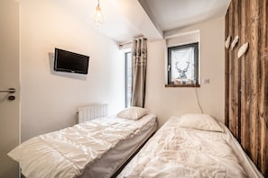 Un dormitorio con dos camas individuales, un televisor montado, una ventana con cortina y una pared de madera.