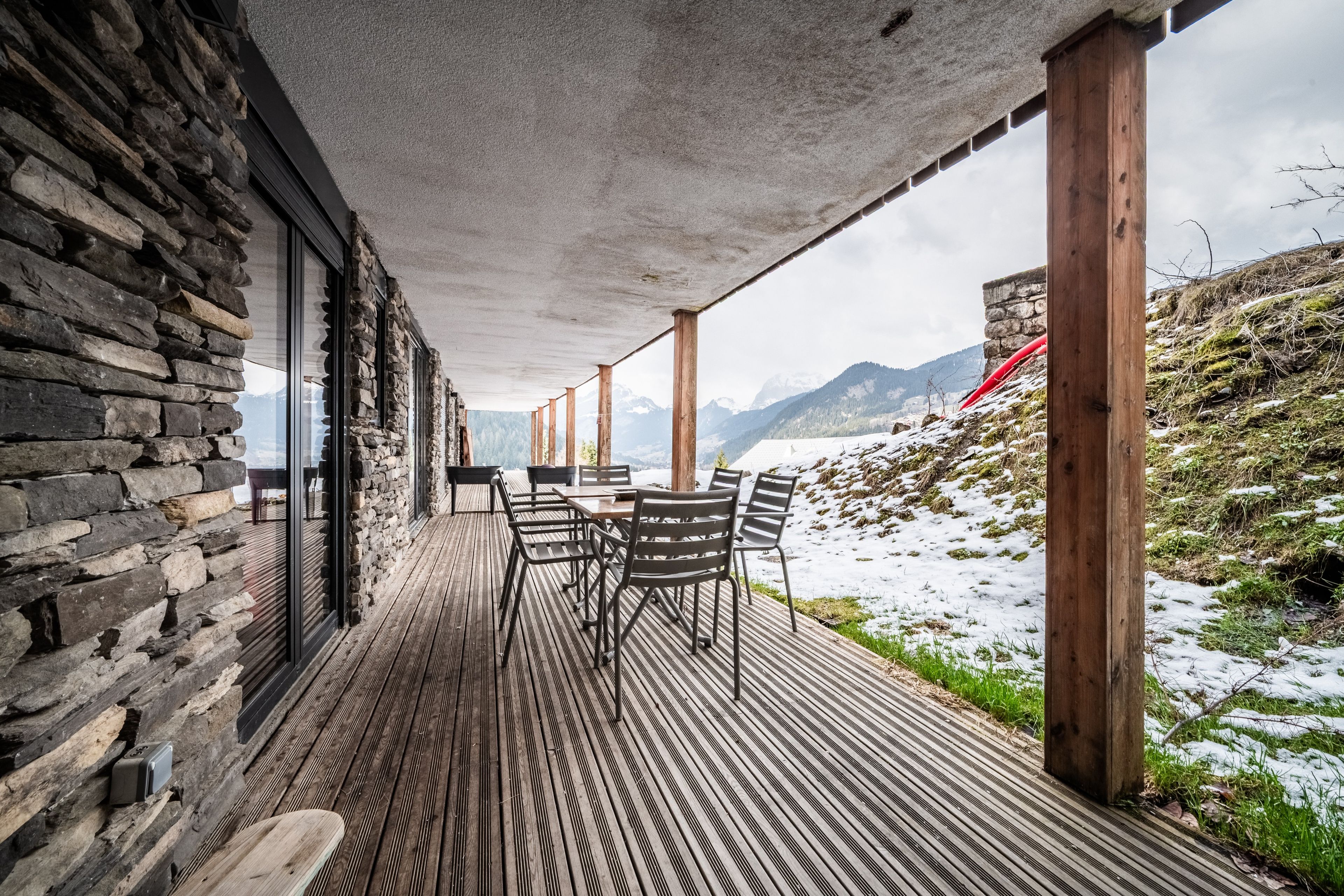 Eine Holzterrasse mit einer Steinsäule und Blick auf einen verschneiten Berg.