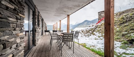 A wooden deck with a stone wall and a view of a snowy mountain.