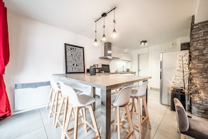Una cocina moderna con una isla central, taburetes de bar, iluminación colgante y una pared de acento de piedra.