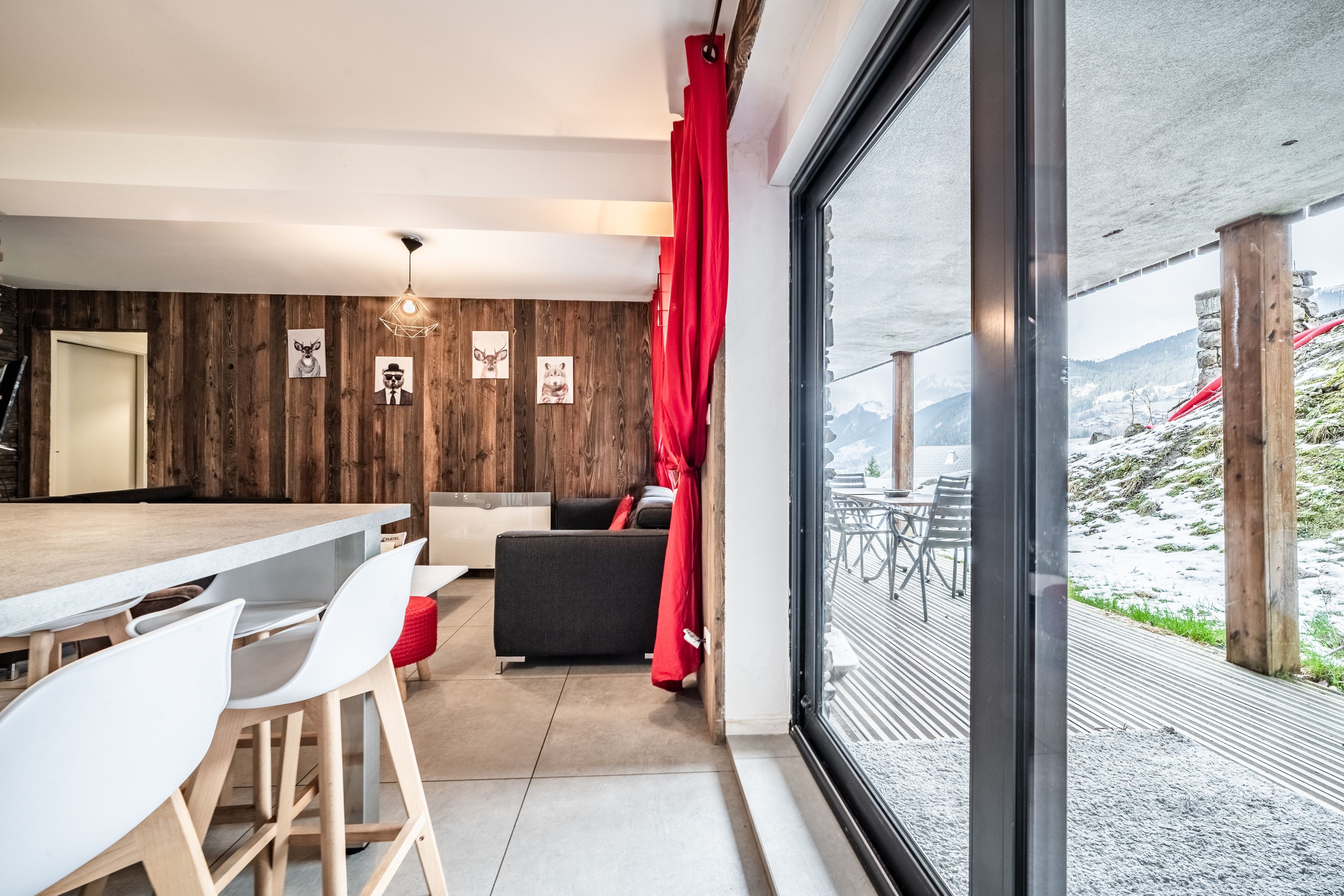Un intérieur moderne comprenant un coin repas, un canapé et une grande fenêtre donnant sur un paysage enneigé.