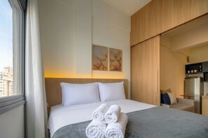A hotel room with a bed, a bedside table, a wardrobe, and a view of the city. - Studio W/ Sea & City View in Downtown Ana1107 (Florianópolis)