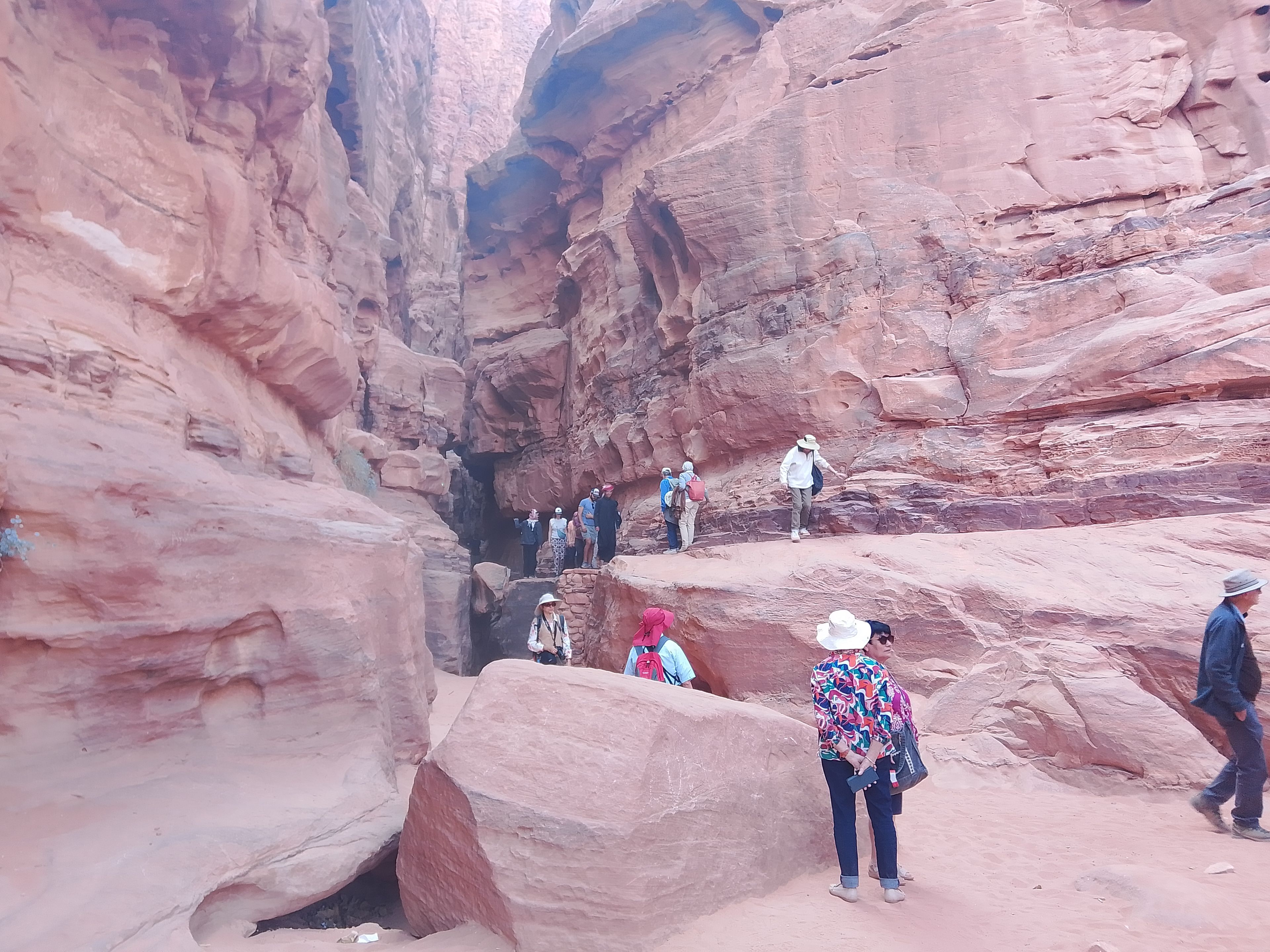 A group of people hiking in a narrow canyon with red rock formations.