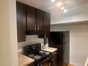 A compact kitchen with dark cabinets, a black stove, and a refrigerator. - Cozy 1-bedroom apartment with AC in Central Houston (Houston)
