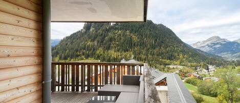 A wooden balcony with a view of a forested mountain.