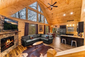 A spacious cabin interior with a fireplace, a large black sectional sofa, a dining area, and a kitchen. - Bear Mountain Hideaway~Theater Room~Game Room~Hot-Tub (Sevierville)
