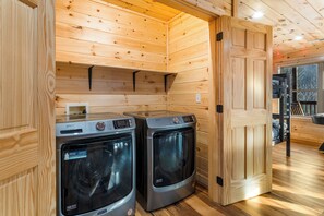 A compact laundry room with two Maytag washers and dryers, wooden walls, and a door leading to another room. - Bear Mountain Hideaway~Theater Room~Game Room~Hot-Tub (Sevierville)
