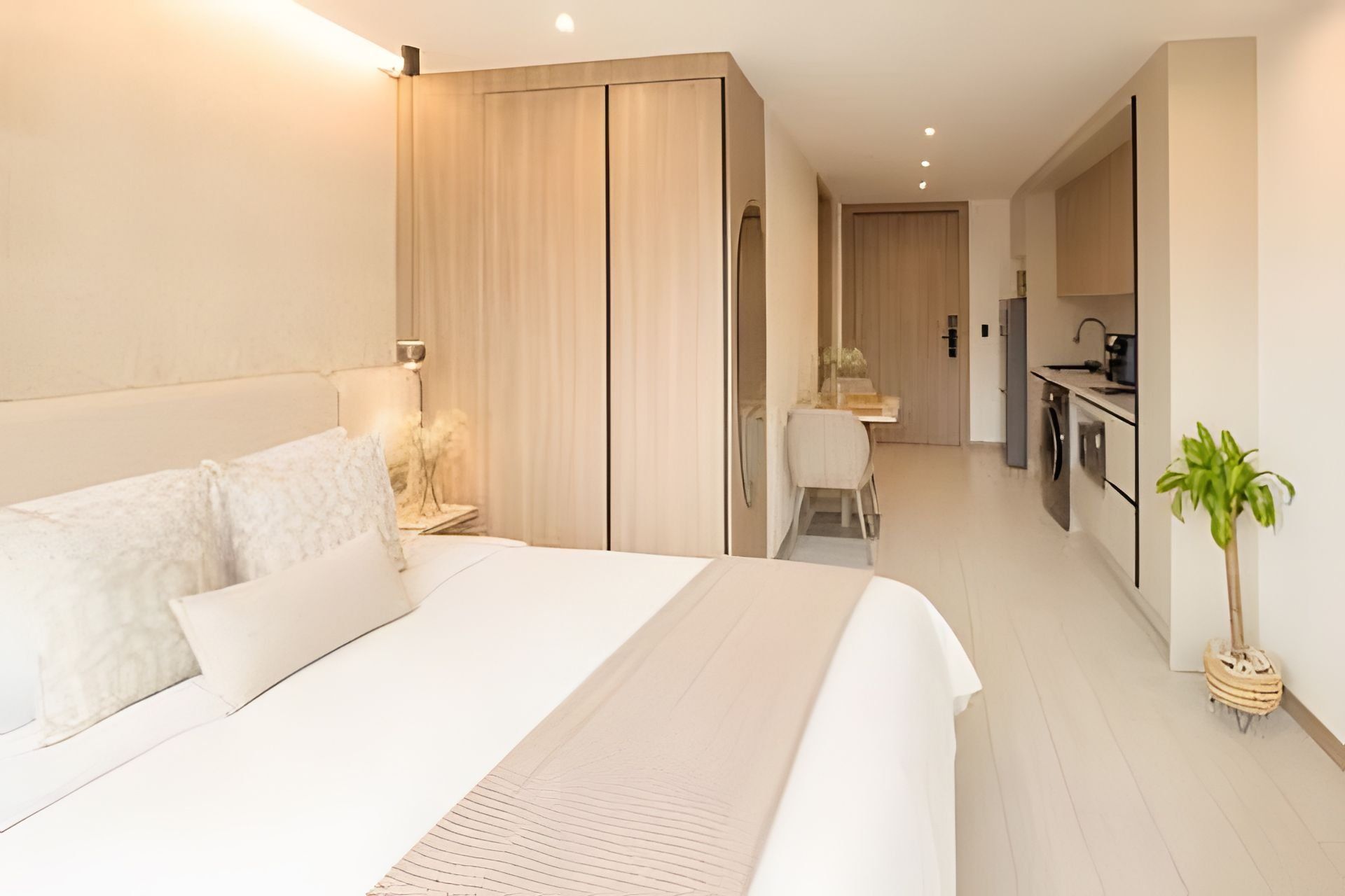 A modern hotel room with a large bed, a desk, and a kitchenette.