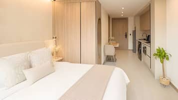 A modern hotel room with a large bed, a desk, and a kitchenette.