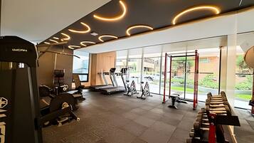 Een sportschool met trainingsapparatuur, grote ramen en uitzicht op buiten.