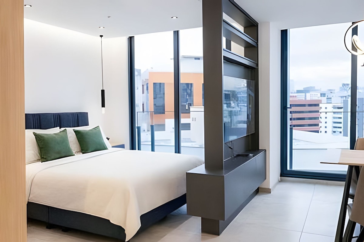 Una habitación de hotel moderna con una cama grande, un televisor de pantalla plana y vistas a la ciudad.