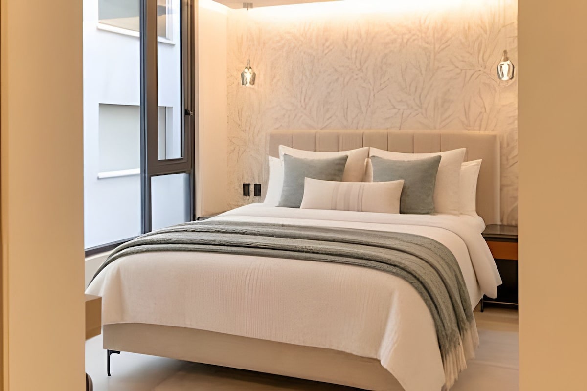Un dormitorio con cama, almohadas, un edredón y una pared con diseño de árbol.