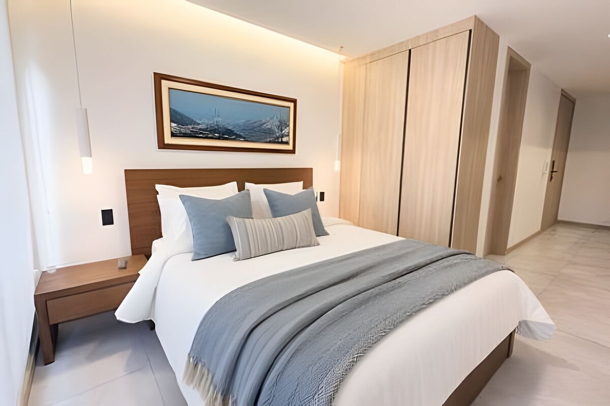 Un dormitorio moderno con una cama grande, una mesita de noche, un armario de madera y un cuadro enmarcado en la pared.