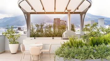 Une terrasse sur le toit, dotée d’un espace salon couvert, de plantes en pot et offrant une vue sur le paysage urbain et les montagnes.