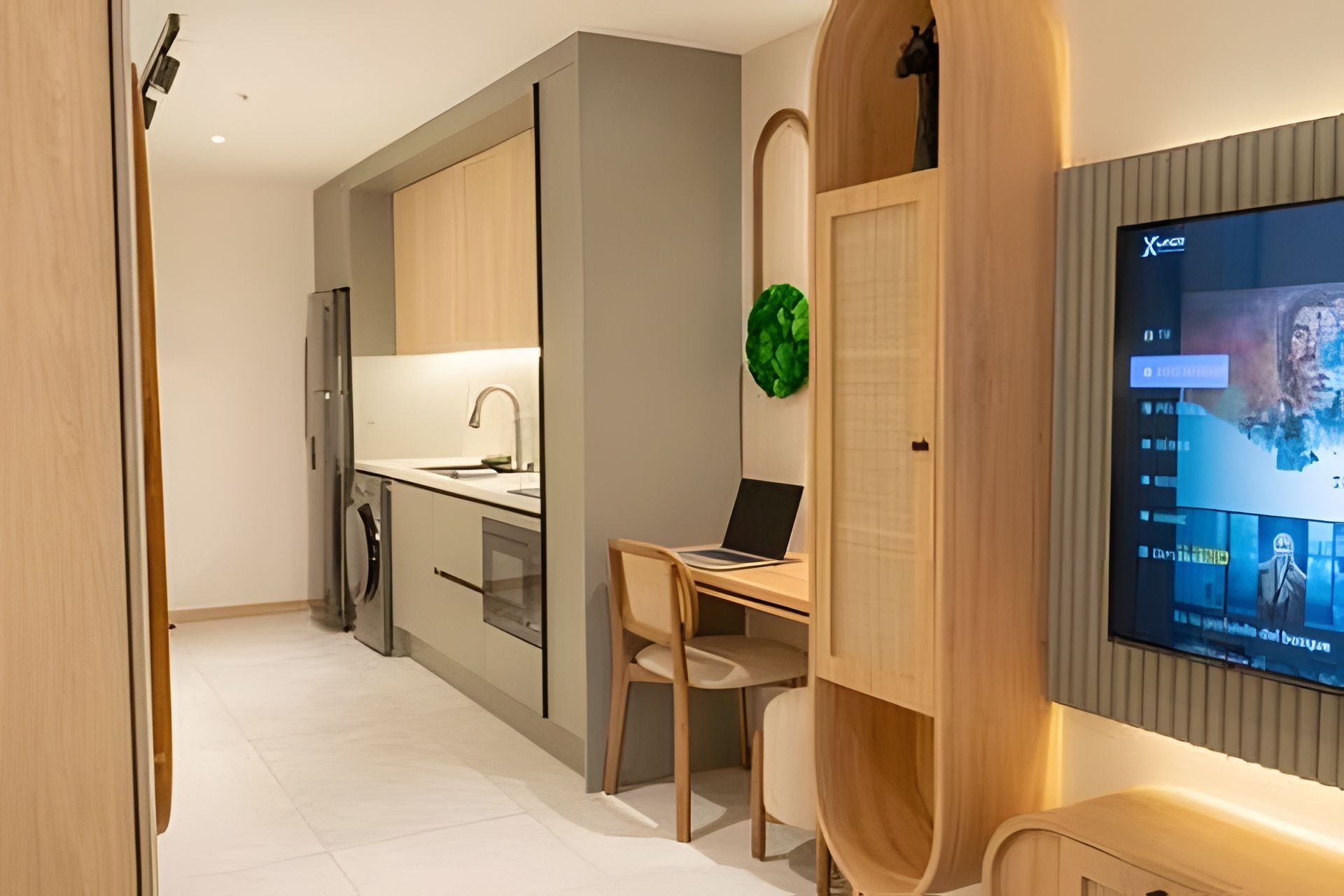 A modern kitchen with a built-in oven, a dining area with a laptop on the table, and a TV mounted on the wall.