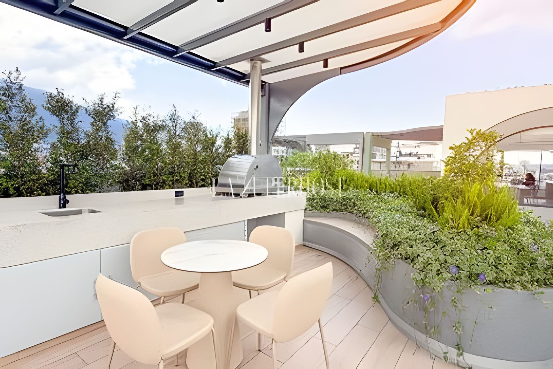 An outdoor patio with a round table and chairs, a grill, and a planter with greenery.