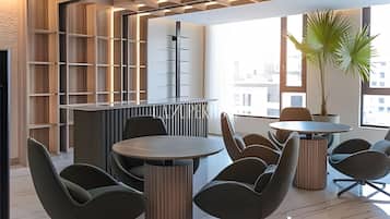 A modern interior with round tables and chairs, a bookshelf, and a large window with a view of buildings.