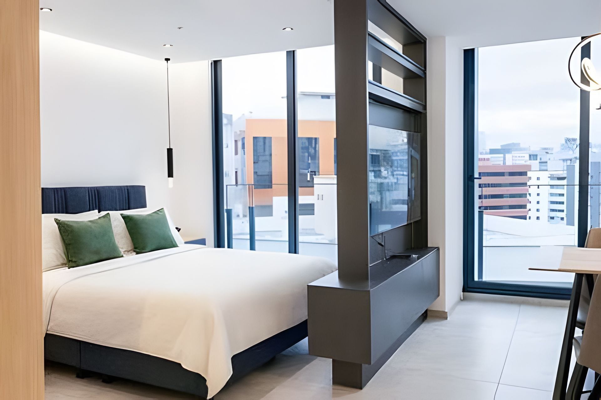 A modern hotel room with a large bed, a flat-screen TV, and a city view.