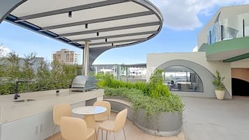 An outdoor patio with a covered seating area, a grill, and a view of the cityscape.